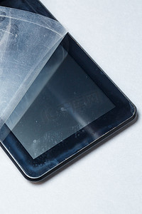 电影划痕摄影照片_黑色划痕平板电脑，灰色背景上有保护膜。