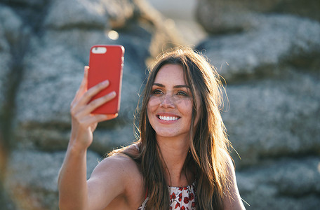 日落真实摄影照片_日落时，美丽的女人在海滩上用智能手机拍照