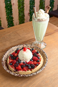 美味的冰淇淋华夫饼，配有红色水果、樱桃和木桌上的奶昔。