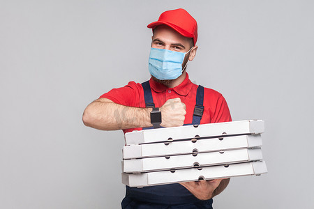 工会背景摄影照片_送货员整体站立，拿着一堆灰色背景的纸板披萨盒。