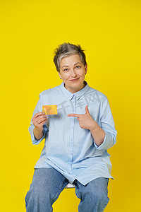 灰白的头发摄影照片_头发灰白的成熟女性手里拿着信用卡、借记卡和平板电脑，进行网上支付或网上购物，隔离在黄色背景中。