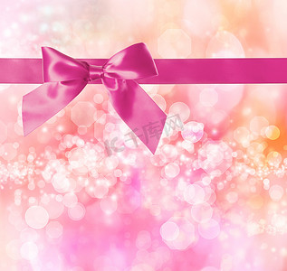 粉红蝴蝶结摄影照片_带有粉红色散景灯的粉红色蝴蝶结和丝带