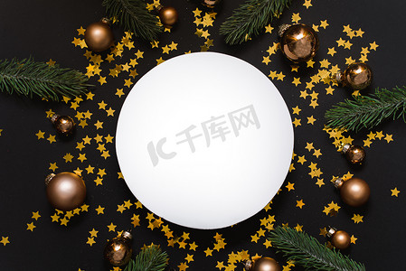 黑色圣诞背景摄影照片_黑色圣诞背景下设计师的白色模型，配有金色球、五彩纸屑和圣诞树枝。
