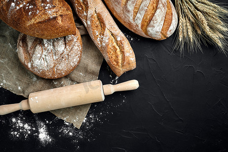 法式长棍面包、烤面包、面粉和小麦穗组合物的顶视图，深色背景上撒有小麦粉