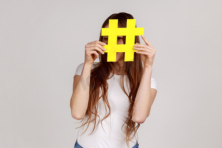 人气标签摄影照片_躲在黄色标签符号后面的女人，用哈希符号遮住脸，互联网上的病毒话题。
