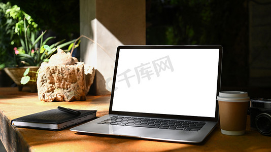 创意户外广告摄影照片_户外咖啡馆木桌上有空白屏幕、咖啡杯和笔记本的笔记本电脑。