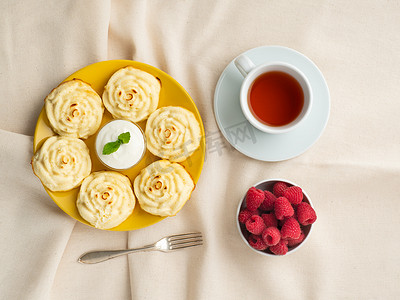 奶酪黄摄影照片_减肥奶酪煎饼，玫瑰形状，黄盘上有茶，覆盆子在纺织亚麻餐巾上