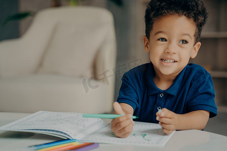 可爱的非洲裔美国小男孩穿着深蓝色马球 T 恤在家画着色书