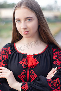 临夏民族大剧院摄影照片_迷人的乌克兰年轻女子在户外穿着民族红色和黑色刺绣连衣裙。