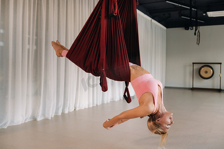 一名年轻女孩，一名空中瑜伽教练，挂在瑜伽俱乐部大厅的吊床上。