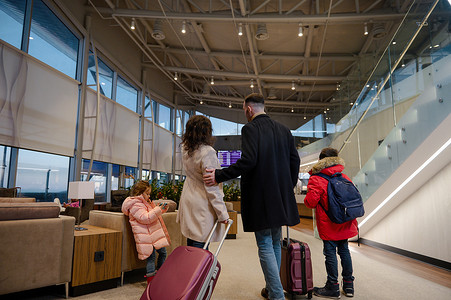 带着手提箱的旅行家庭检查机上航班信息和时间表，站在机场出发航站楼，等待登机