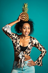 顽皮的年轻非洲裔美国女性，头戴新鲜菠萝，作为蓝色工作室背景的皇冠。