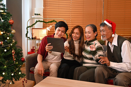 美丽的家庭在数字平板电脑上进行视频通话，坐在装饰精美的房间里庆祝新年和圣诞佳节