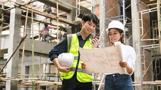 发展计划摄影照片_戴安全帽的建筑师团队在施工现场共同讨论工业建筑设计项目工作计划