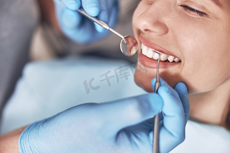 自信的成熟医生正在现代诊所检查年轻美丽快乐白人女性的牙齿