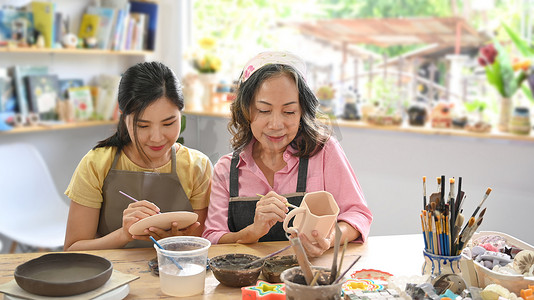 年轻妇女和退休妇女在陶器作坊烘烤前在碗上画画