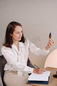 芳香治疗师女孩坐在办公室里，手里拿着一瓶芳香油，正在写下一些东西。