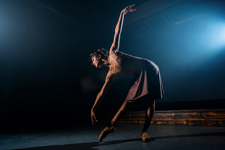 优雅的芭蕾舞演员穿着古典或现代芭蕾舞元素，在黑暗中用泛光灯背光跳舞。