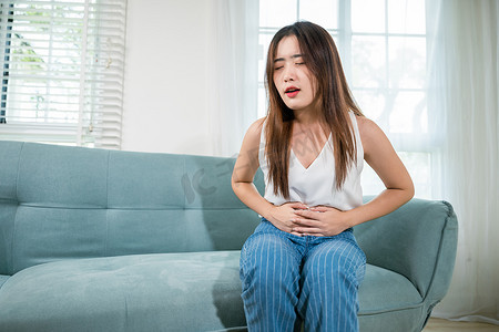 亚洲年轻女性不高兴的手握着腹部疼痛的胃