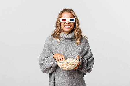 戴着 3D 眼镜看电影、吃爆米花、站在白色背景上的迷人快乐女孩
