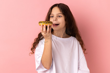 高兴可爱的小女孩舔着美味的甜甜圈，看起来渴望吃甜点。