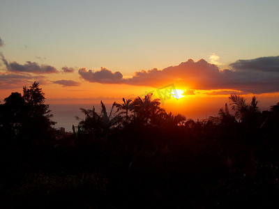 从坦塔罗斯山看到的日落穿过海洋上的云层，经过热带树木的剪影