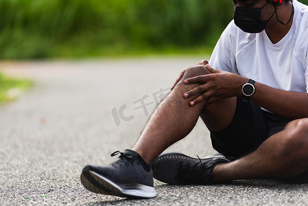 他在跑步摄影照片_跑步的黑人男子戴着手表坐着，他在跑步时用手关节握住膝盖