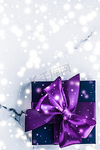 紫色的雪花摄影照片_冬季节日礼盒，配有紫色丝绸蝴蝶结、大理石背景上的雪花，作为豪华美容品牌的圣诞和新年礼物，平铺设计