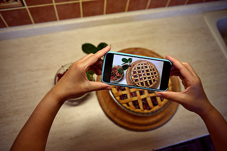一位女性美食博主的手拿着智能手机，拍着经典的美国酥皮樱桃派的照片