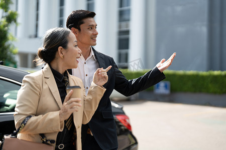 快乐的高级亚洲老女商人在停车场与年轻的亚洲男同事讨论新项目。