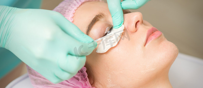 年轻女子在美容院接受睫毛去除手术，并用棉签和棒去除睫毛膏。