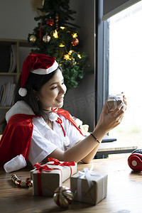性格开朗的年轻女子戴着圣诞老人的帽子，拿着包装好的礼物盒。