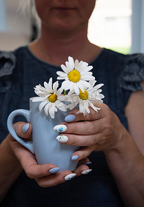 一位年轻女子拿着一杯蓝色的雏菊，这是美丽的夏日美甲