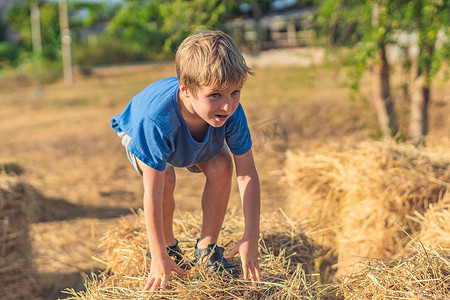 男孩蓝色 T 恤微笑着爬上干草堆的干草堆，晴朗的天空阳光灿烂的日子。
