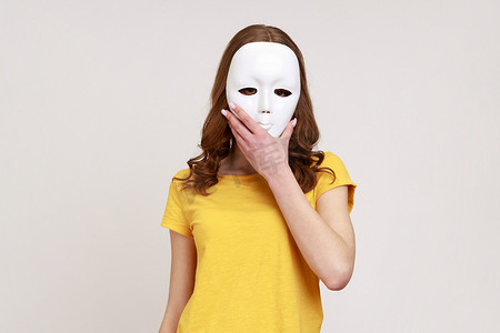 身着黄色休闲风格 T 恤的身份不明的女性，用白色面具遮住脸，隐藏个性、阴谋和隐私。