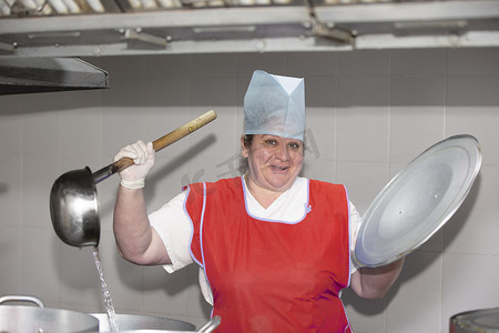 一名女工在工业厨房里做饭，金属锅里放着一个大勺子。