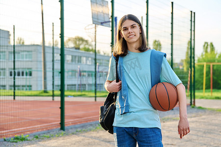 户外篮球场附近背着背包球的学生肖像