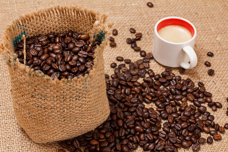 咖啡豆跌落摄影照片_一杯咖啡和烘焙过的咖啡豆装在帆布袋里。