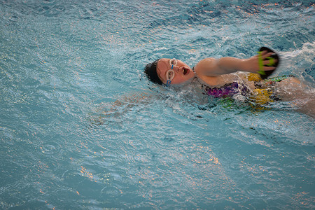 游泳泳镜摄影照片_戴着泳帽和泳镜的女孩在游泳池里。
