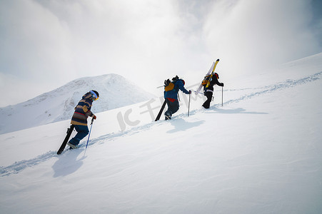 三个朋友滑雪者手里拿着滑雪板和滑雪板上坡，进行野外或自由滑雪