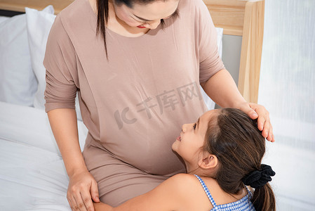 可爱的女儿拥抱妈妈，听妈妈肚子里婴儿的声音，检查和看着妈妈的脸。