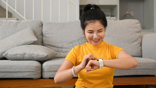 健身教练摄影照片_运动型亚洲女性在家锻炼时休息并检查智能手表上的心率数据