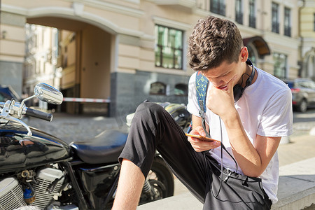 男孩青少年 16,17 岁，使用智能手机，坐在夏季城市的街道上