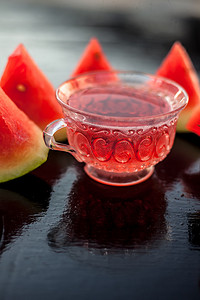 在木质表面的透明玻璃杯中垂直拍摄西瓜籽果冰茶以及​​三角形西瓜片。