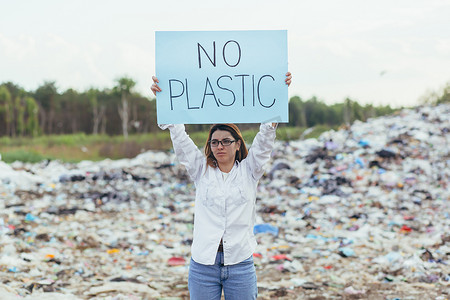 海报保护环境摄影照片_女志愿者在垃圾填埋场举着无塑料海报，积极分子与环境污染作斗争