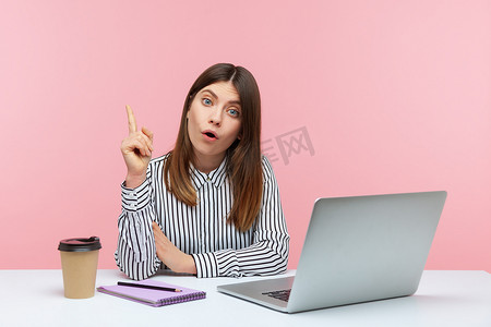 知性摄影照片_情绪化的年轻女性坐在粉红色背景的办公室里工作。