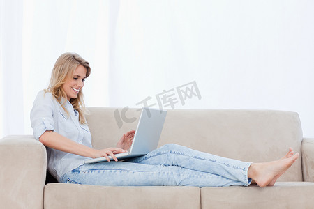 一位女士躺在沙发上用笔记本电脑打字