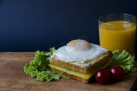 健康的三明治，配有奶酪和容易煎的鸡蛋，放在木板上，配有沙拉、番茄和橙汁。