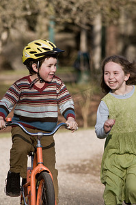 他在跑步摄影照片_男孩骑自行车，女孩在他旁边跑步