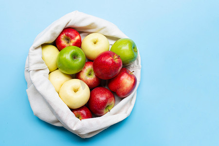 奶奶种地摄影照片_蓝色背景布袋中新鲜多汁的苹果。
